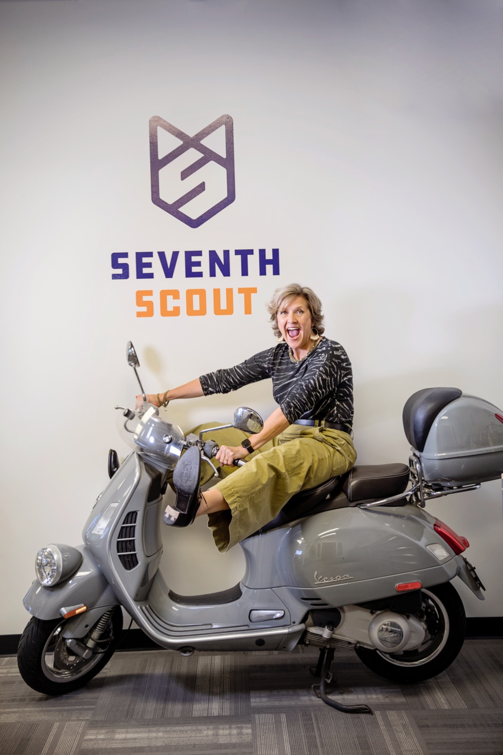 Lynn Yeldell laughing on a Vespa beneath the Seventh Scout logo