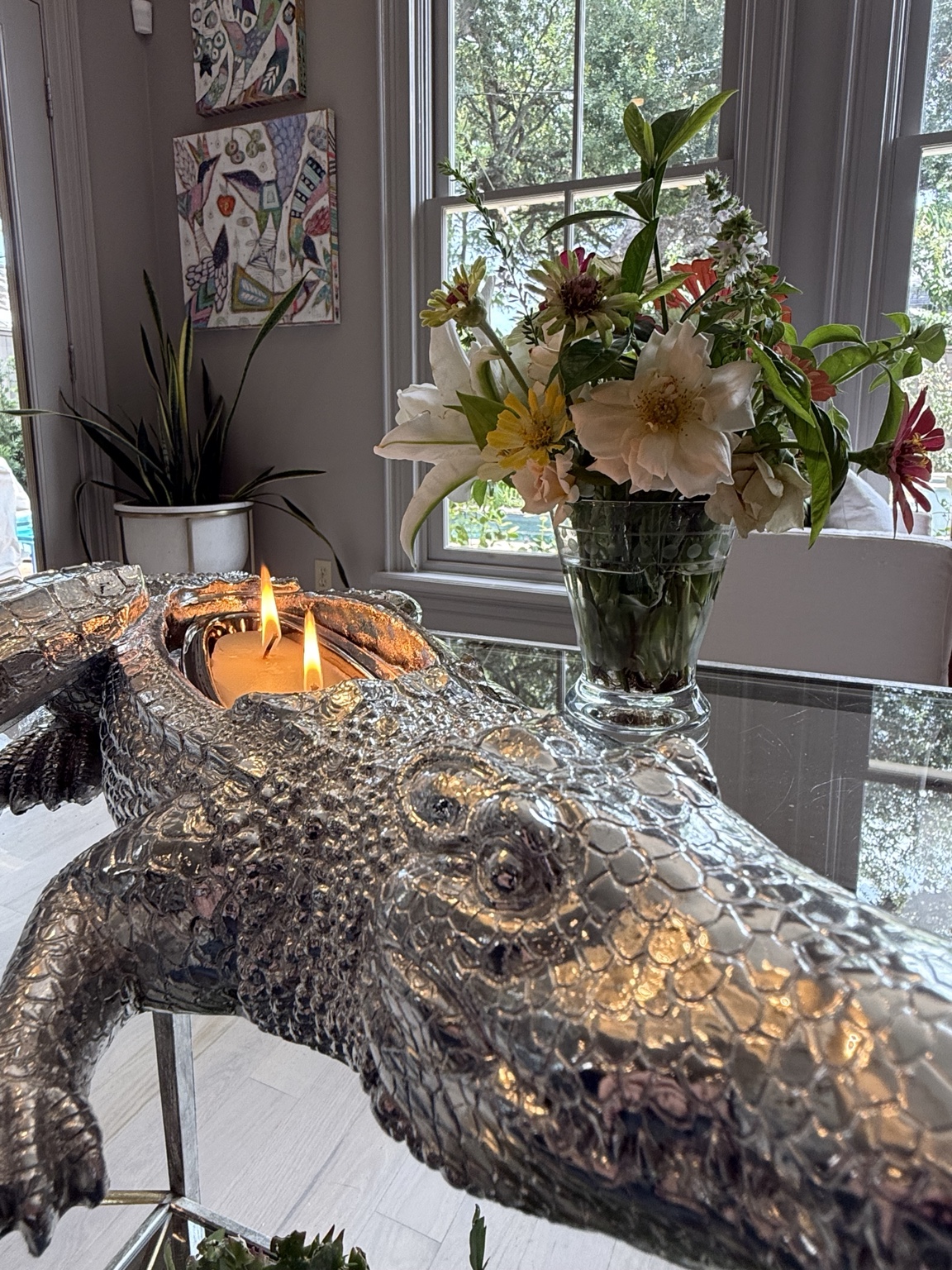 The silver alligator candle glowing beside fresh flowers